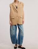Person wearing a beige blazer, black top, blue jeans, and black shoes on a white background